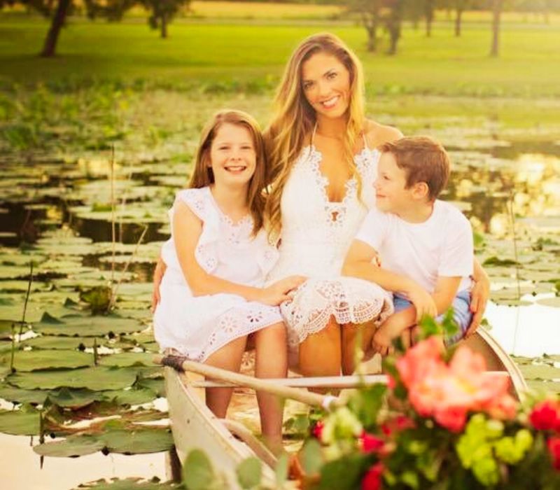 A woman and two children smiling while sitting in a canoe surrounded by water lilies.